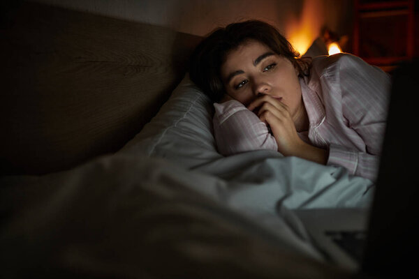 Женщина размышляет о своих чувствах, лежа в постели поздно ночью, окруженная тусклым светом.