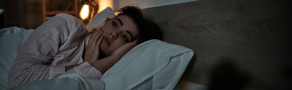 A woman lies in bed, lost in thought, battling the weight of her emotions in a quiet room.