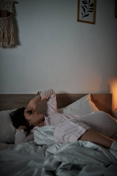 Женщина лежит на кровати, борясь с сильными эмоциями в мягком вечернем свете.