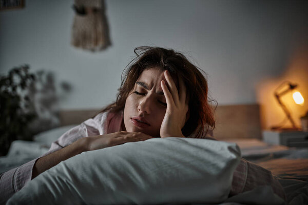 A woman lies in bed, overwhelmed by heavy emotions in the stillness of morning.
