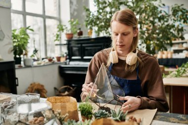 Katılımcı, yemyeşil bitkilerle çevrili eğlenceli bir atölyede sulu düzenlemeler yapar..