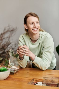 Atölyede uzun saçlı, şık giyinmiş, gülümseyen bir adam..