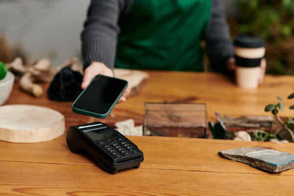 Young person with phone using payment terminal in a vibrant green setting.