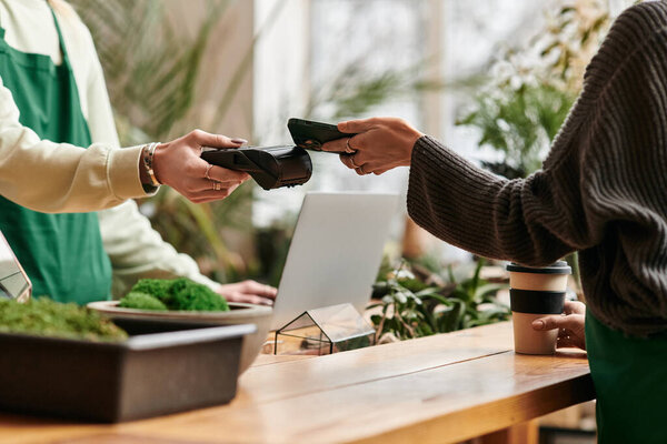 Stylish woman paying with her phone while man working in green setting.