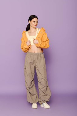 Güzel genç bir kadın, parlak turuncu ceketi ve rahat pantolonuyla moda anlayışını sergiliyor..