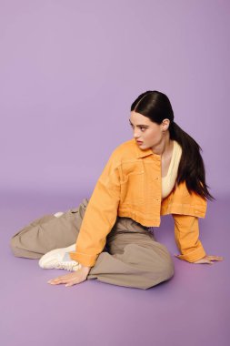 Genç bir kadın zarif bir şekilde yerde oturuyor, şık kıyafetini göz alıcı bir şekilde sergiliyor.