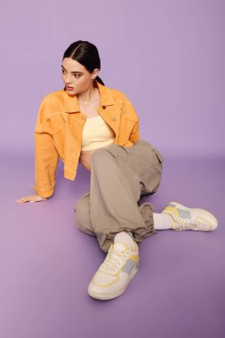 Genç bir kadın, mor bir arka planda moda anlayışını renkli bir elbiseyle sergiliyor..