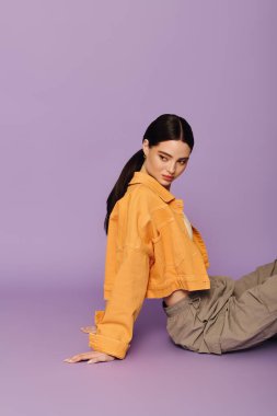 Canlı ceketli, kendine güvenen genç bir kadın, rengarenk mor bir arka plana karşı poz veriyor..