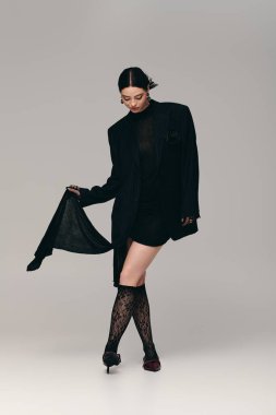 Zarif bir siyah elbise giyen genç bir kadın, hareketlerinde özgüven ve zarafet ifade eder.