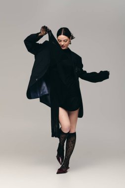 Güzel, genç bir kadın, kendine güvenerek şık kıyafetini oyuncu bir pozla sergiliyor..