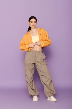 A young woman showcases contemporary fashion with a trendy outfit while striking a pose in a studio. clipart