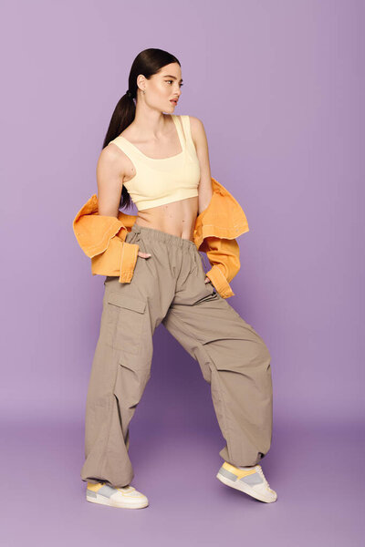 Молодая и стильная женщина стоит с руками в карманах, одетая в удобную, но шикарную одежду.