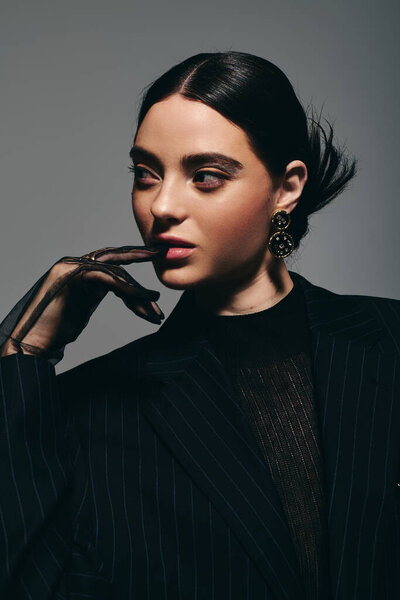 A young stylish woman gazes thoughtfully while elegantly posing in an artistic setting.