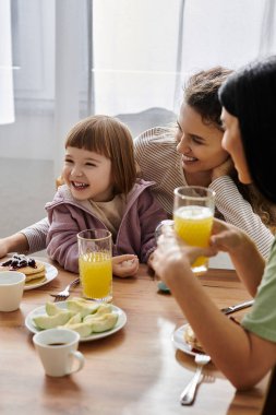 İki neşeli kadın ve kızları birlikte keyifli bir kahvaltı yapıp, kahkahalarını ve sevgilerini paylaşıyorlar..