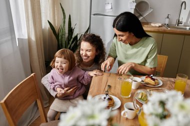 İki kadın, neşeli kızlarıyla birlikte, neşeli ve modern bir mutfakta, mutlu bir kahvaltı yapıyorlar..