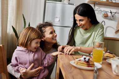 İki neşeli kadın, kızlarıyla gözleme ve kahkaha paylaşıyor. Sıcak, modern bir yerde..