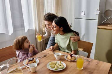 İki kadın, kahvaltıdan zevk alırken kızlarıyla sevgi dolu bir şekilde iletişim kurar..