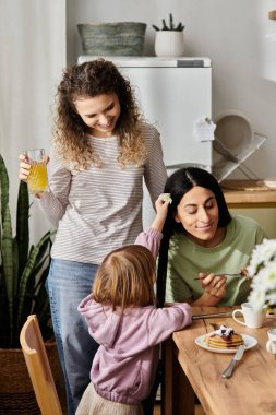 İki sevgi dolu kadın, kızlarıyla güzel bir dairede kahvaltı yapıyorlar..