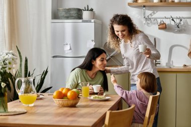 Two women share a joyful moment with their daughter in a cozy, modern apartment setting. clipart