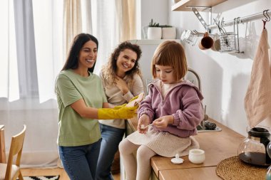 Two women enjoy a cheerful moment with their daughter in their stylish home. clipart