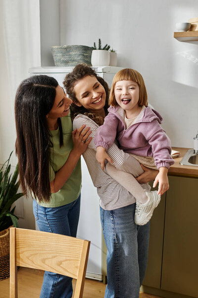 Две любящие женщины делятся радостным смехом со своей маленькой дочерью на яркой кухне.