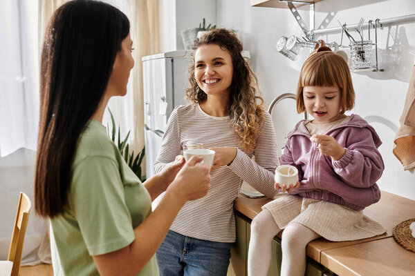 Две женщины смеются вместе со своей дочерью, наслаждаясь уютным моментом в своей квартире.