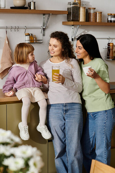 Две женщины делят радостные моменты со своей дочерью, расслабляясь дома в стильной кухне.
