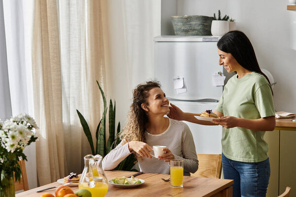 Две веселые лесбиянки делят восхитительный завтрак в своем современном доме, в окружении тепла.