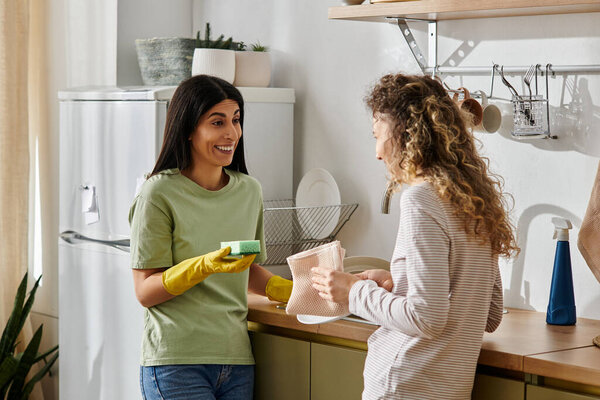 Two happy women engage in house chores, sharing smiles in their cozy apartment together.