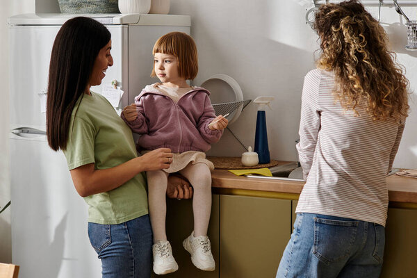 Two women share a joyful moment with their daughter in a stylish kitchen, embracing family life.
