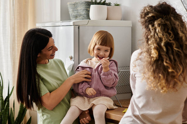 Two women share joyful moments with their young daughter in a stylish home setting.