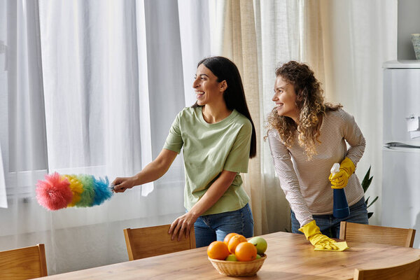 Two happy women share laughter while cleaning their stylish apartment, creating a warm atmosphere.