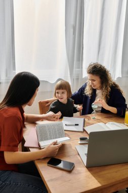 Üç aile ferdi, sıcak evlerinde, ahşap bir masanın etrafında neşeli bir anı paylaşıyor..