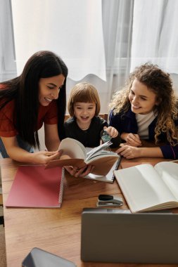 İki sevgi dolu anne evde birlikte kitap okurken kızlarıyla gülüşürler..
