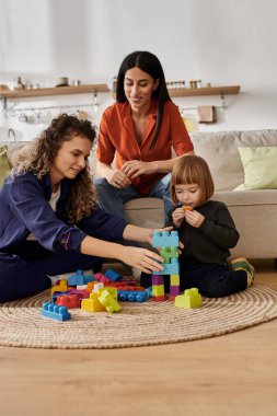 Two women foster their daughter's creativity with colorful building blocks in a cozy home. clipart