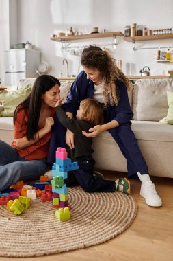 Two women share joyful interactions with their daughter while playing on the floor. clipart