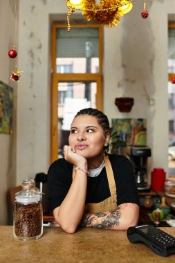 Genç bir kadın, bir kafe tezgahında düşünceli bir şekilde oturur. Etrafı sosyetenin sıcaklığı ve kahveyle çevrilidir..