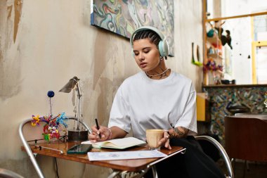 Kulaklık takan genç bir kadın bir kafede içki içerken defterine bir şeyler yazıyor..