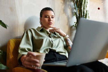Genç bir kadın sıcak bir kafede laptopuyla çalışırken kahvesini yudumluyor..