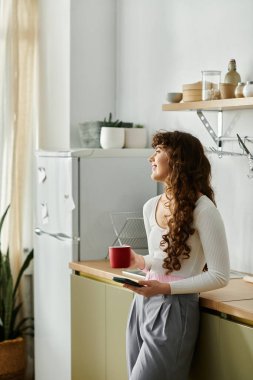 Genç bir kadın mutfak tezgahında sıcak bir içki yudumluyor ve dikkatlice pencereden dışarı bakıyor..