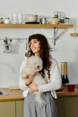Neşeli bir kadın köpeğini şık bir mutfakta sallıyor, havayı neşeyle dolduruyor..