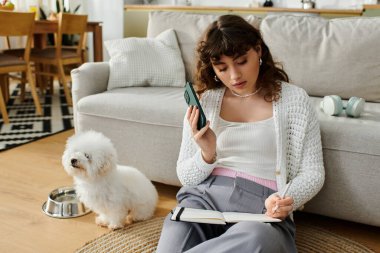 Genç bir kadın defterine yazıp köpeğiyle telefonda sohbet ediyor..