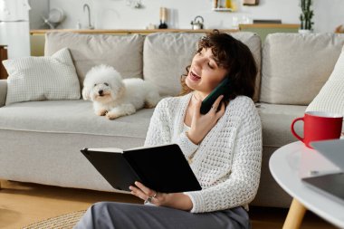Genç bir kadın köpeğiyle evde dinlenirken telefonda gülüyor ve konuşuyor..
