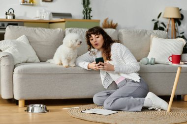 Genç bir kadın rahat bir katta oturuyor, akıllı telefonuyla meşgul, köpeği de merakla izliyor..