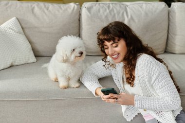 Akıllı telefonuyla meşgul olan genç bir kadın, kabarık tüylü arkadaşıyla neşeli bir anı paylaşıyor..