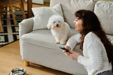Genç bir kadın kanepede gevşiyor, kabarık köpeğiyle şakalaşıyor, sıcaklık yaratıyor..