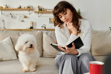 Genç bir kadın, köpeği yakından izlerken kanepede bir defter yazar..