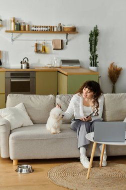Genç bir kadın, modern bir yaşam alanında sevimli köpeğiyle oynarken kanepesinde dinleniyor..