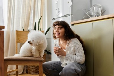 Genç bir kadın yerde diz çöker, içkisi ve tüylü köpeğiyle gülümser..