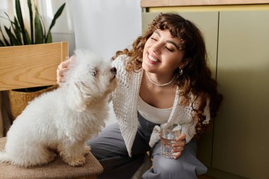 Güneşli bir odada, genç bir kadın gülüyor ve tüylü köpeğini okşuyor, sıcak, neşeli bir atmosfer yaratıyor..